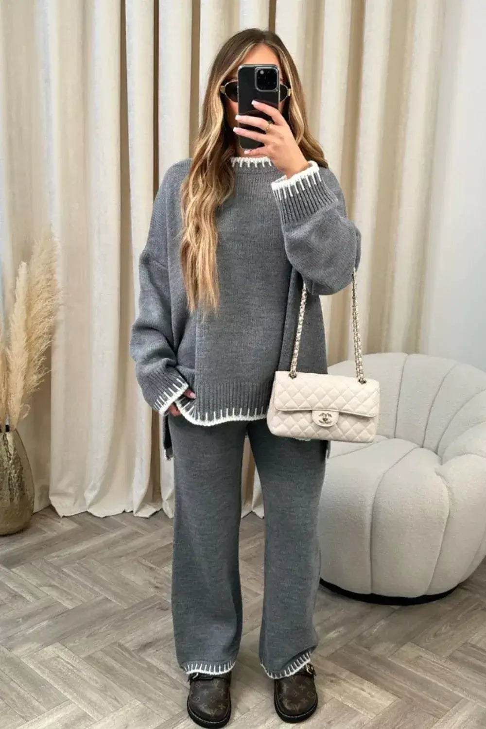 Woman modeling a contrast trim knit set featuring a round neck top and matching pants, styled with a handbag.