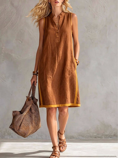 A woman in a brown sleeveless dress with a V-neck and button-front design, holding a stylish tote bag.