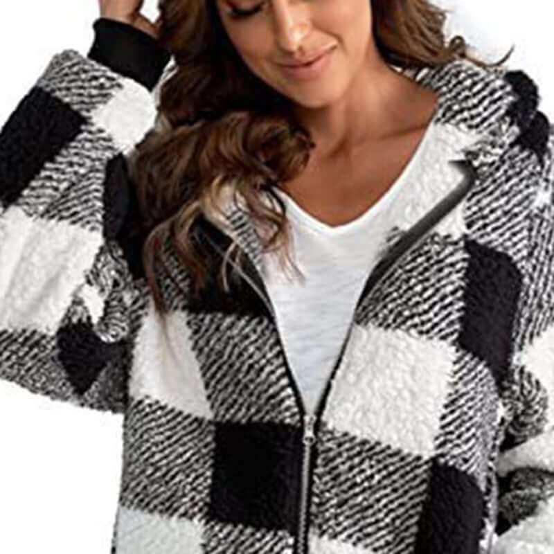 Woman wearing a plaid oversized winter jacket with a hood, featuring black and white patterns and a full front zipper.