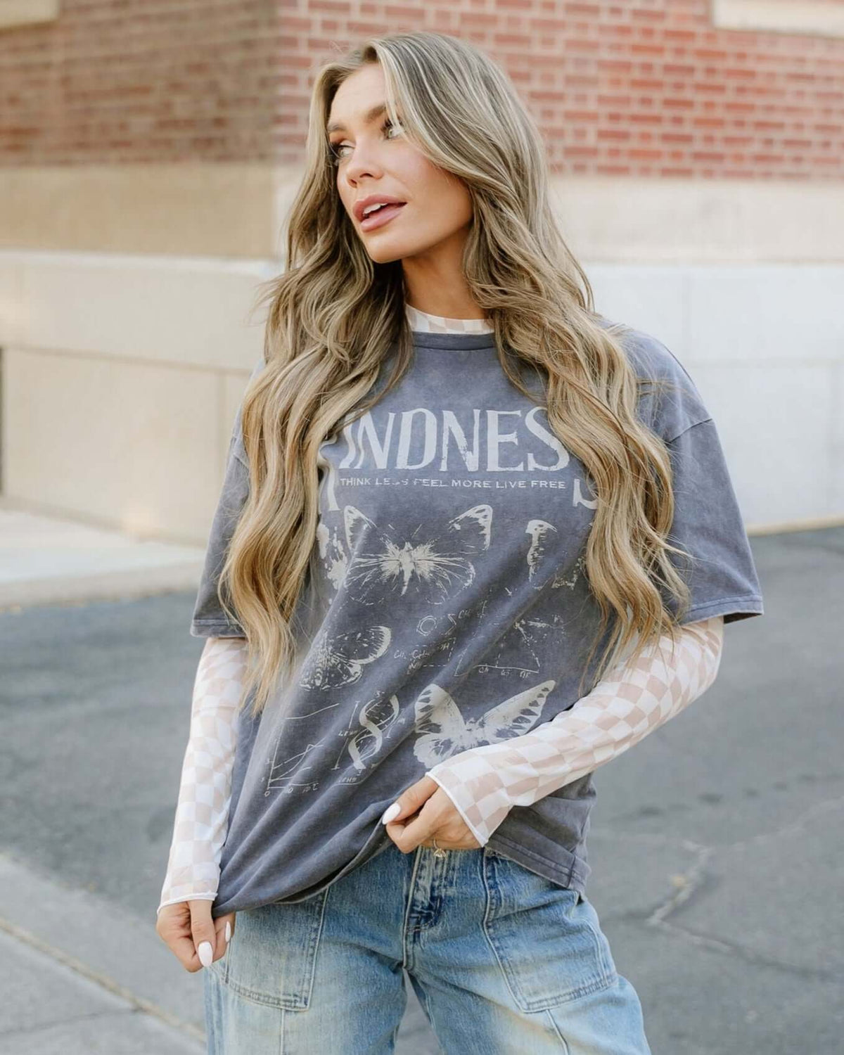 Model wearing a khaki sheer checkered top layered over a graphic tee, styled with casual jeans.