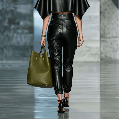 Model walking in PU leather streetwear pants with elastic waist, stylish top, and green handbag.