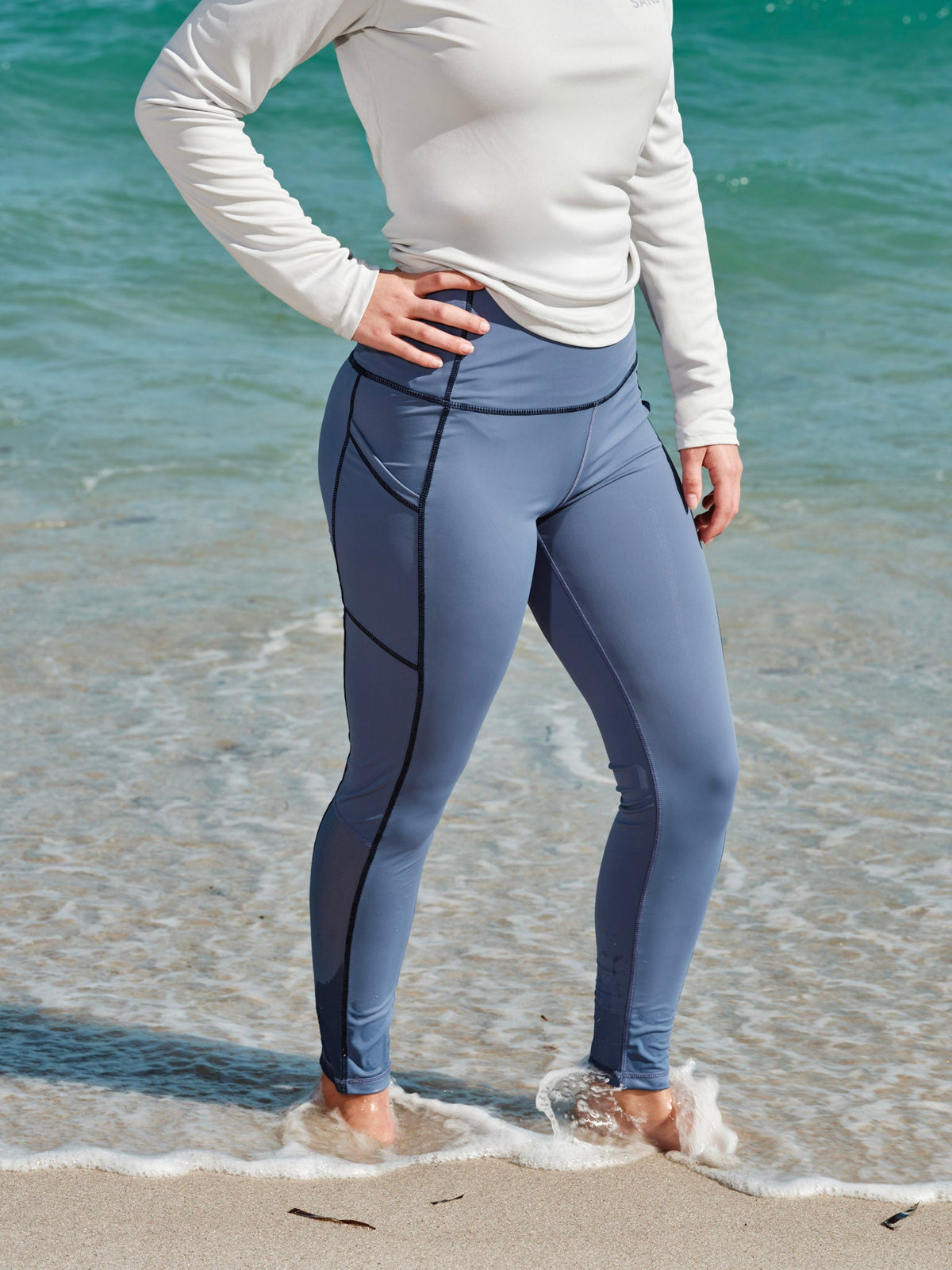 Model wearing high-performance swim leggings by the shore, showcasing style and functionality for outdoor activities.