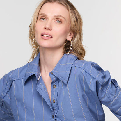 Woman wearing sculptural gold tone pearl hoop earrings with a blue striped shirt.