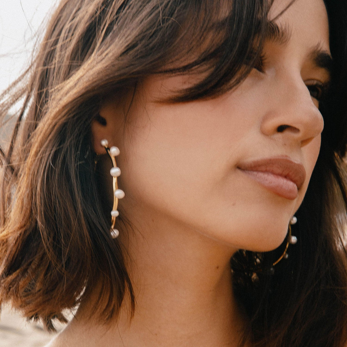 Close-up of a woman wearing gold tone pearl hoop earrings showcasing their sculptural design and freshwater pearls.