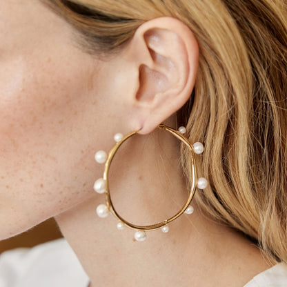 Gold tone pearl hoop earrings showcasing a sculptural design with asymmetrical freshwater pearls for modern elegance.