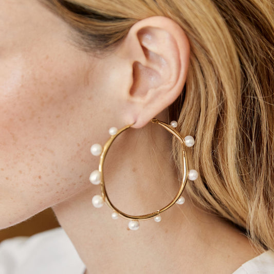 Gold tone pearl hoop earrings showcasing a sculptural design with asymmetrical freshwater pearls for modern elegance.