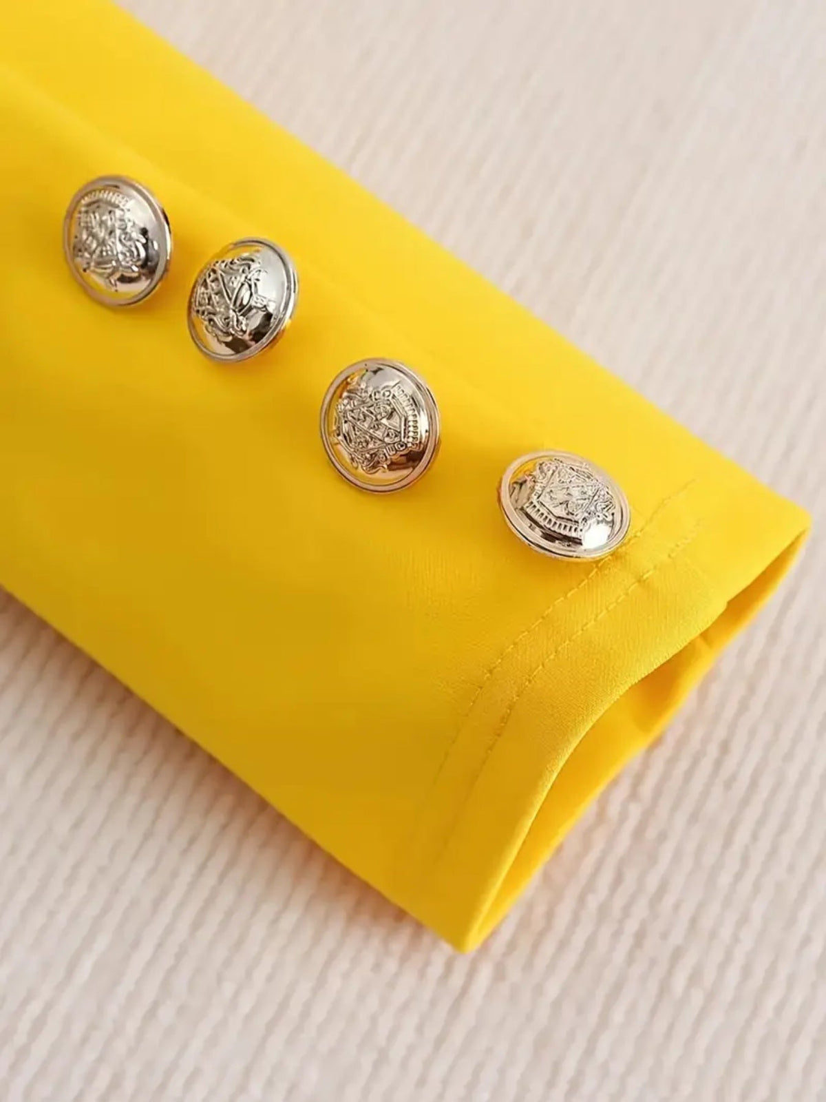 Close-up of silver buttons on a vibrant yellow sleeve of a womens printed pants suit.