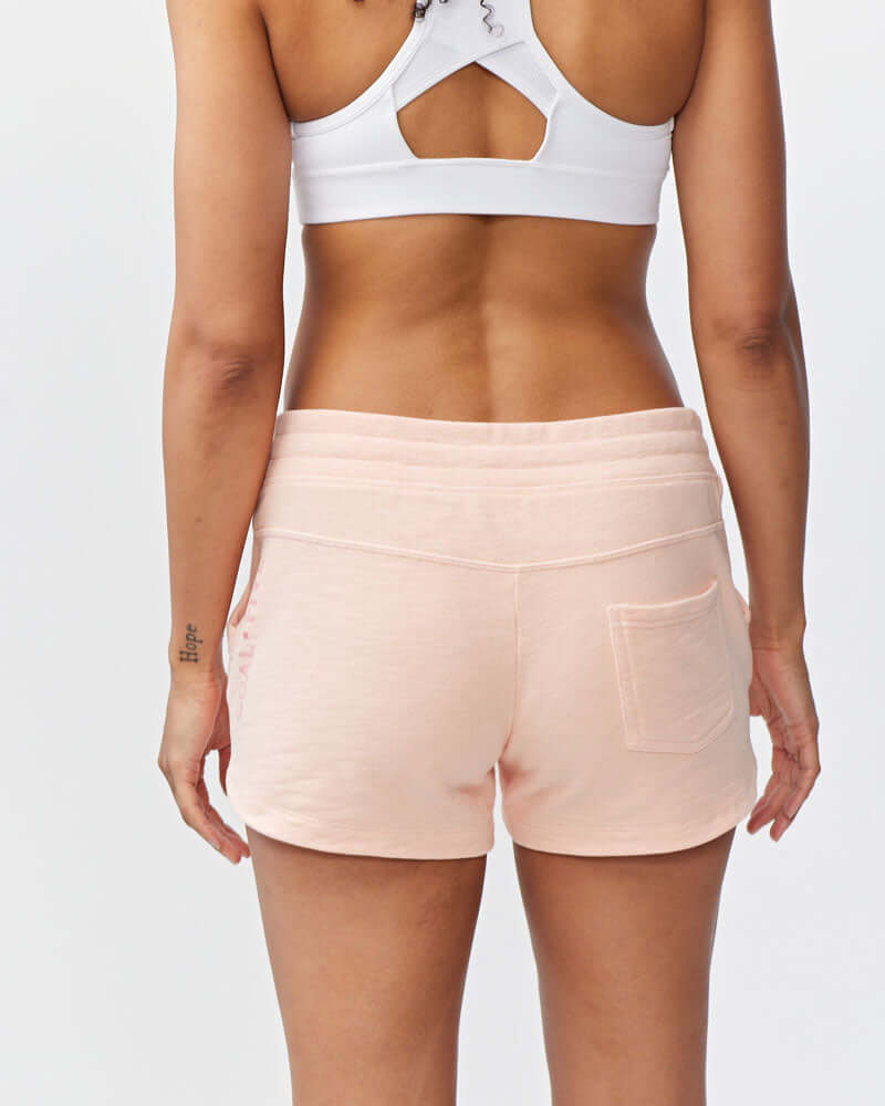 Woman wearing Freasy Garment-Washed Cotton Shorts in soft pink, showing back view with rib-knit waistband.